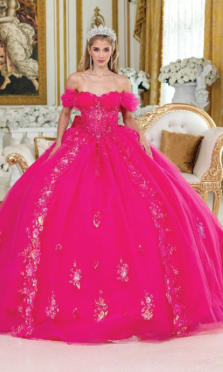 A woman in the Quinceanera Dress 5006 By Dancing Queen, featuring a fuchsia pink corset bodice and floral details with a tiara, stands in an ornate room with gold accents.